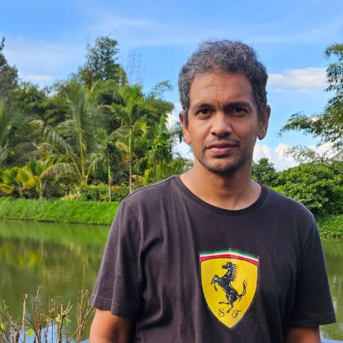 Kartik Singh standing by a lake, with palm trees and open sky behind him.